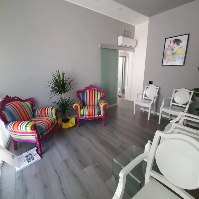 La sala d'attesa appena aperta, con due poltrone barocche a righe colorate, sedie bianche e un tavolino in vetro.