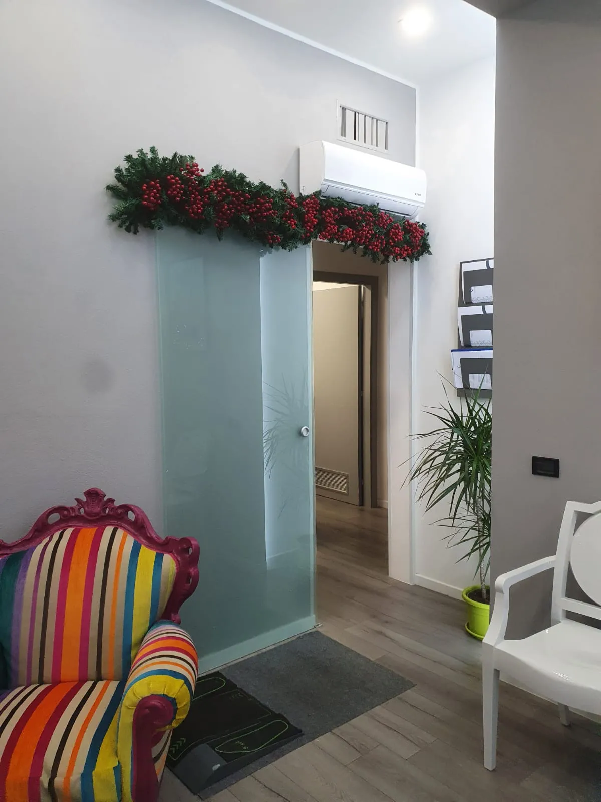Un angolo della sala d'attesa: una poltrona a righe, una sedia bianca, una pianta e la porta in vetro satinato verso le sale.